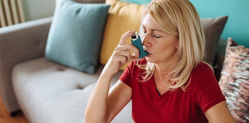 Woman using inhaler while sitting on couch